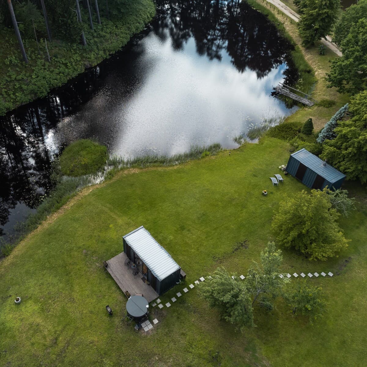 Skats no augšas uz mājiņas teritoriju ar dīķi un mežu